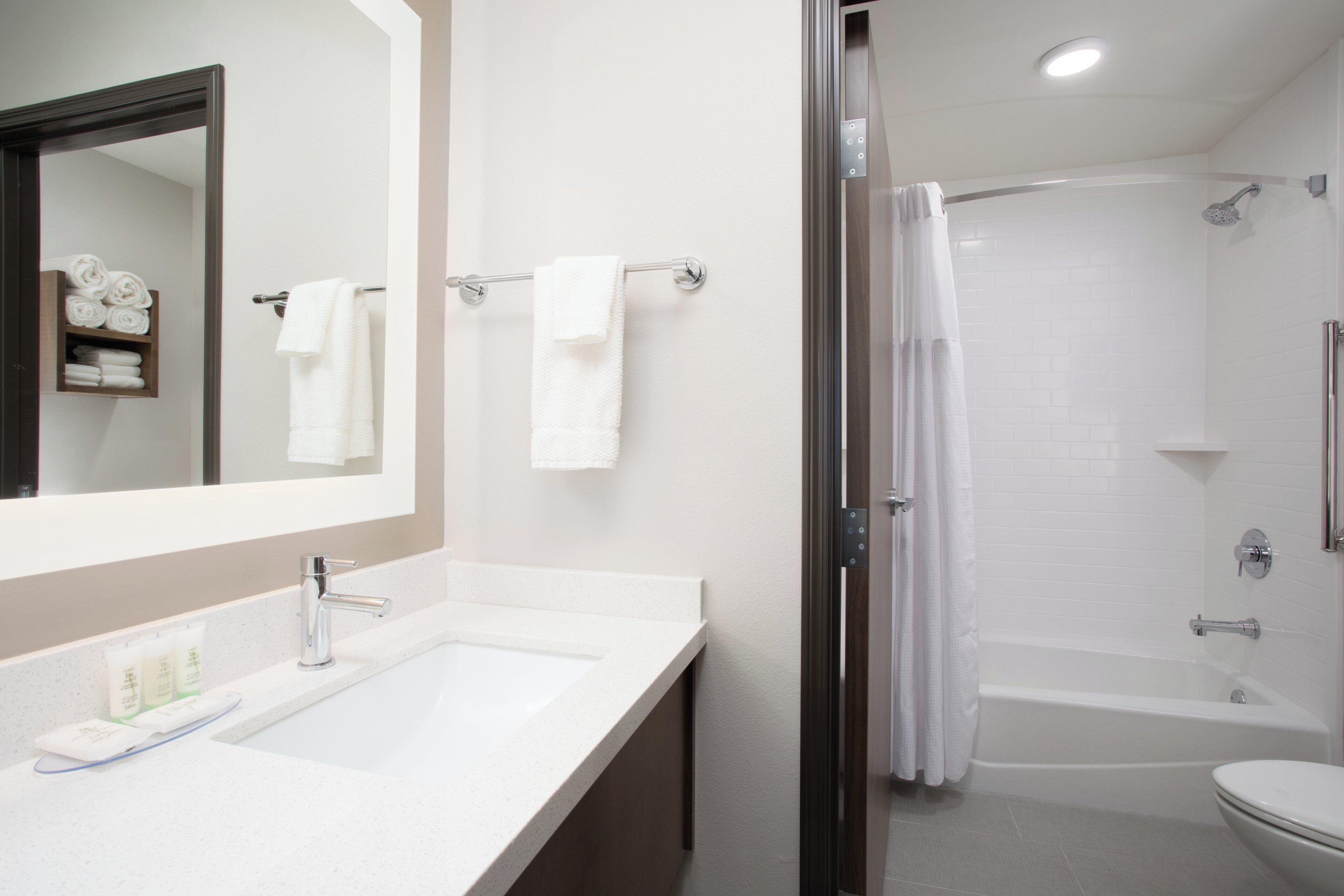 A modern bathroom with a sink, mirror, towel rack, shower, and toilet.