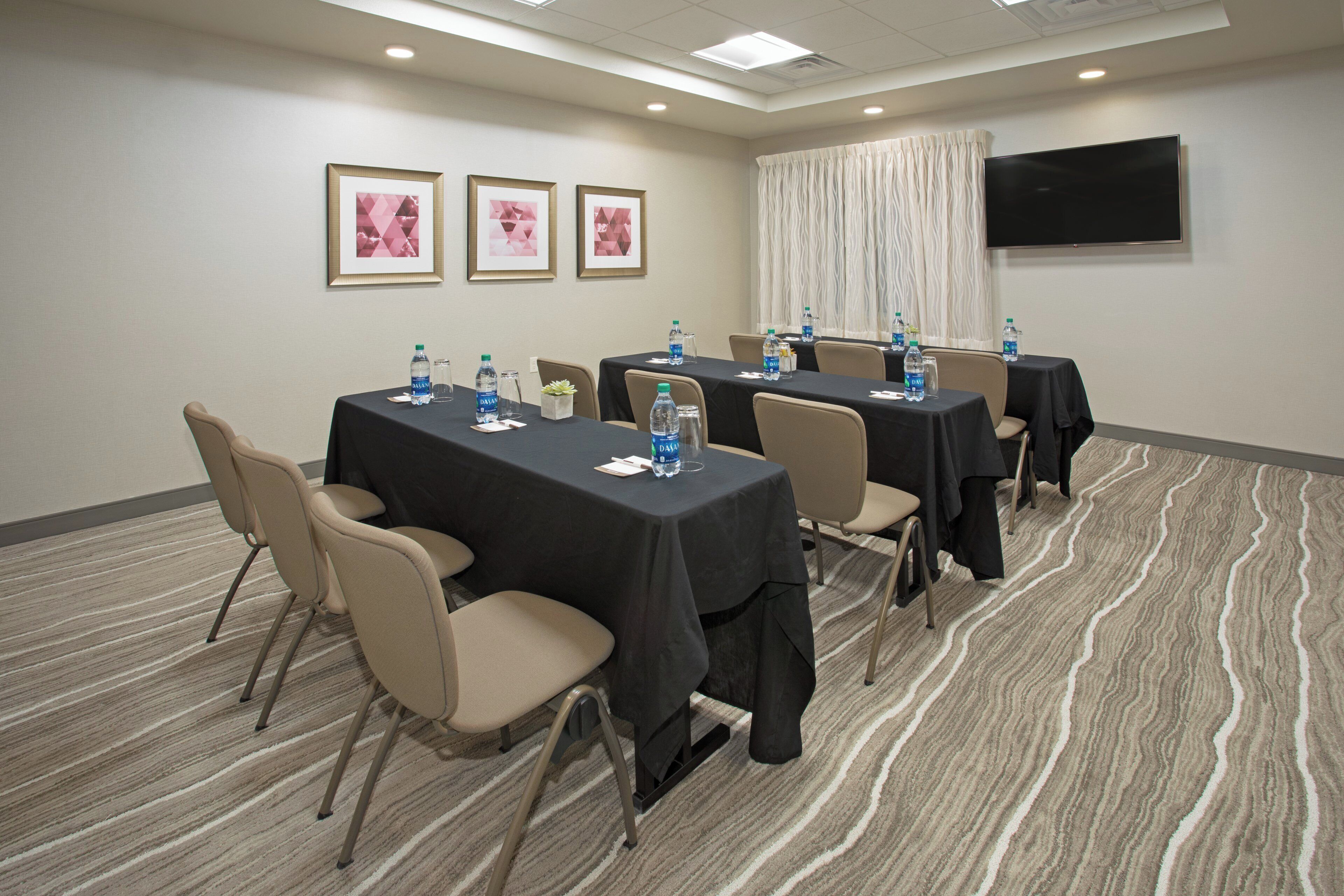 A conference room with tables, chairs, water bottles, and framed pictures on the wall.