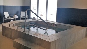 Une piscine intérieure d’environ 90 cm de profondeur, un vestiaire équipé de chaises et une vue sur l’extérieur.