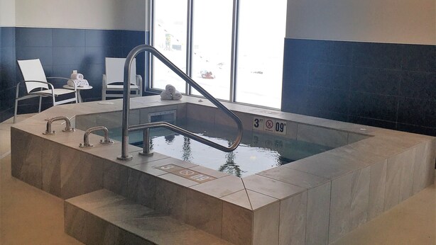 Una piscina interior con una profundidad de 90 centímetros, un vestuario con sillas y vistas al exterior.