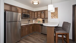 Cocina moderna con electrodomésticos de acero inoxidable, armarios de madera y una barra con un taburete.