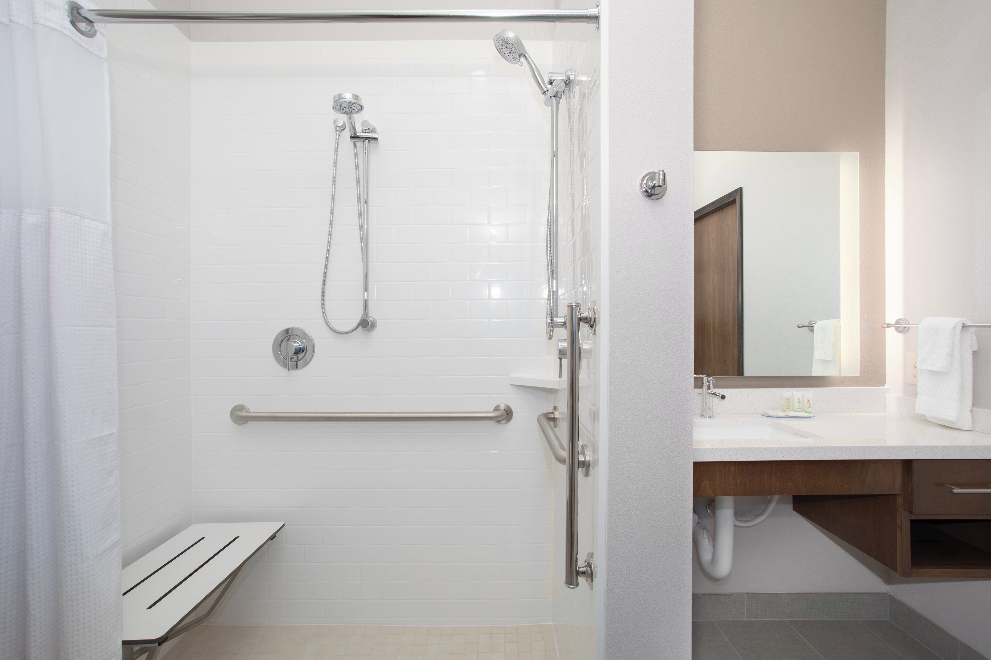 A modern bathroom with a glass-enclosed shower, a white tiled wall, a wooden vanity, and a mirror.