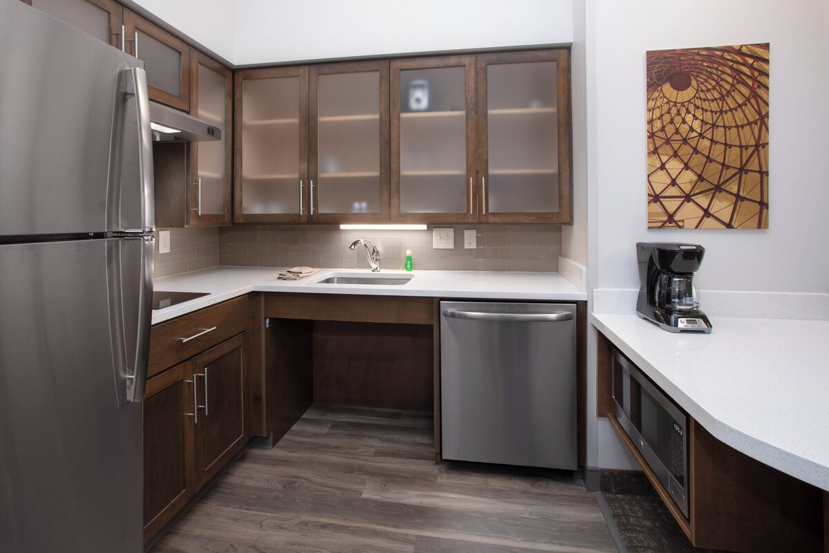 Una cocina moderna con electrodomésticos de acero inoxidable, armarios de madera, lavavajillas y cafetera.