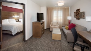 Habitación de hotel con cama, escritorio, sofá, silla, televisor y ventana con cortinas.