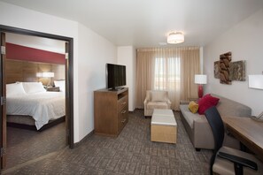 Habitación de hotel con cama, escritorio, sofá, silla, televisor y ventana con cortinas.