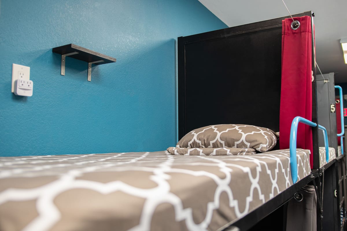 Un lit superposé avec une couvre-lit à motifs, un rideau rouge et une étagère adossée à un mur bleu.