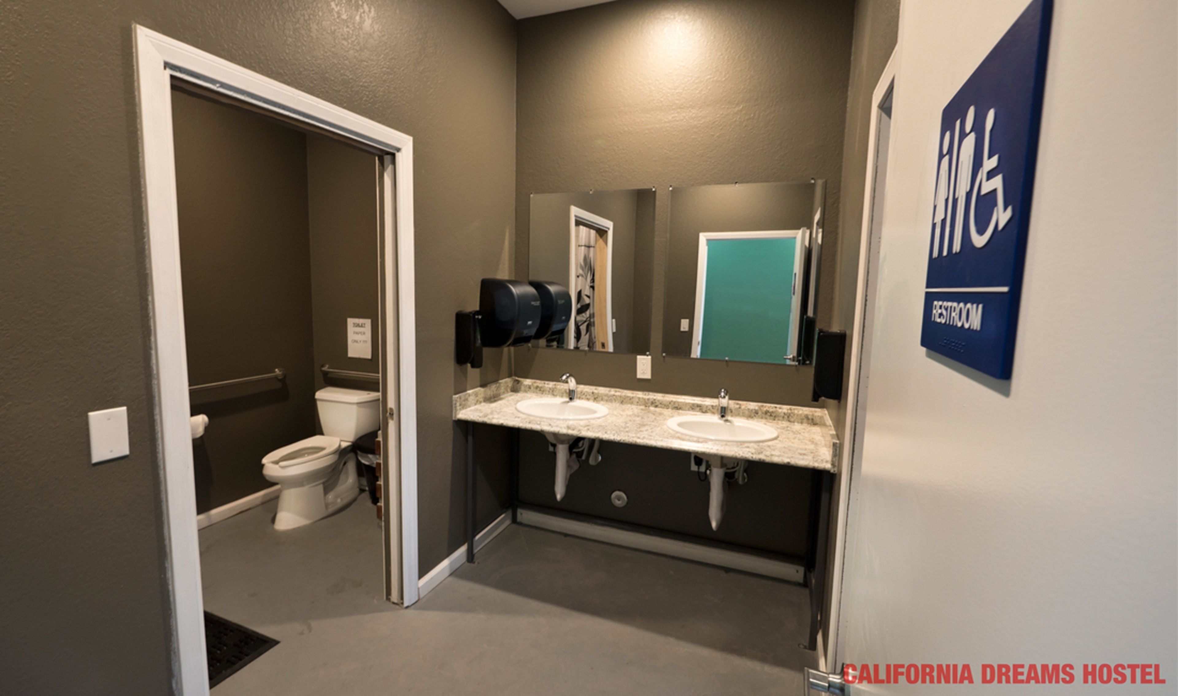 Een badkamer met twee wastafels, een toilet en een papieren handdoekdispenser.
