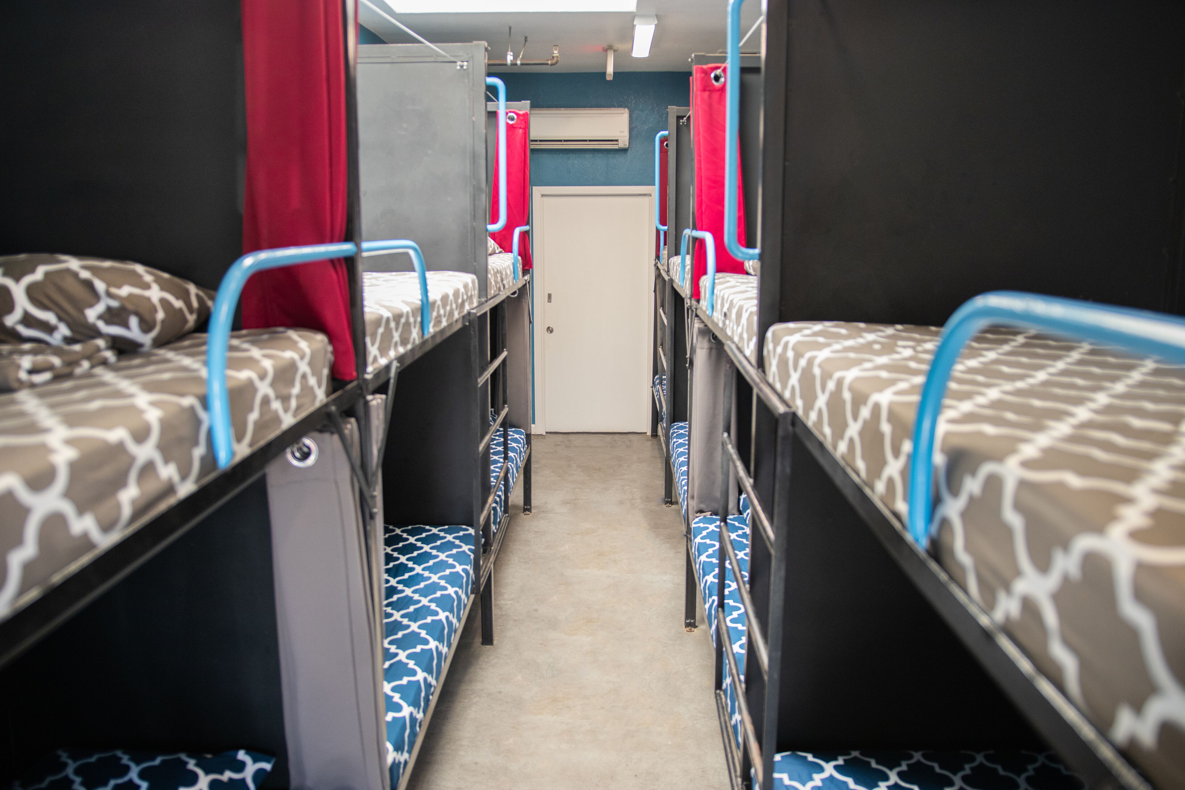 A narrow corridor with bunk beds on either side, a door at the end, and an air conditioning unit on the wall.