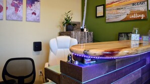 A reception desk with a wooden top and LED lights, a white office chair, and artwork on the walls. - California Dreams Hostel - Pacific Beach (San Diego)