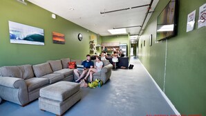 A living area with a sofa, ottoman, and a kitchenette in the background. - California Dreams Hostel - Pacific Beach (San Diego)