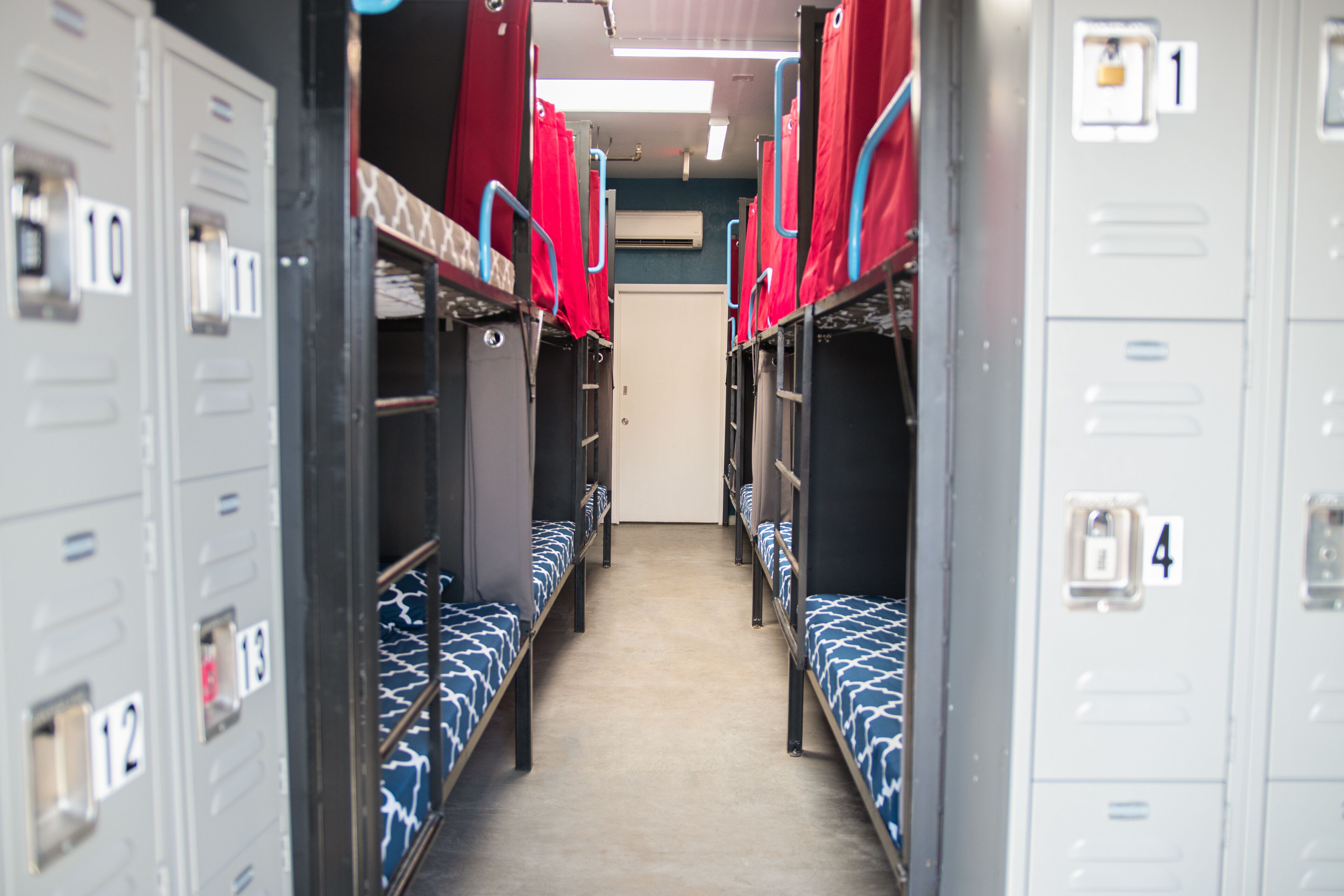 A corridor with bunk beds, lockers, and a door at the end.