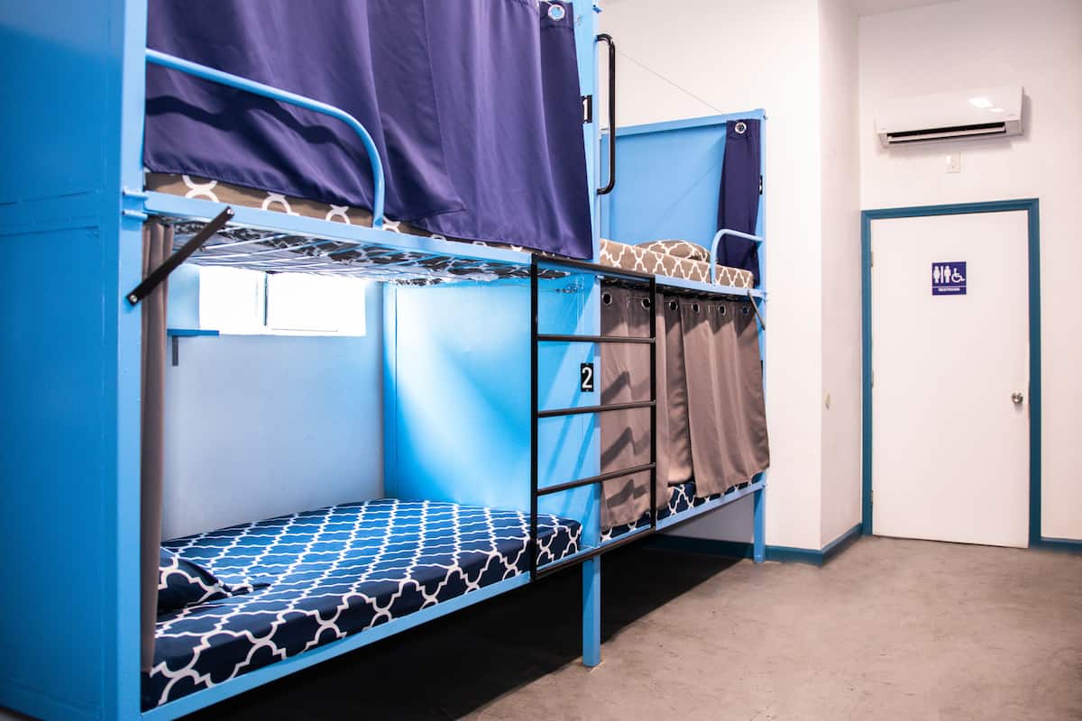 Une chambre avec des lits superposés, dont un lit superposé numéro 2, une porte portant un panneau indiquant qu’elle est accessible aux personnes en fauteuil roulant, et un appareil de climatisation fixé au mur.