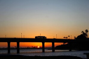 A bridge with a vehicle, palm trees, and a sunset.