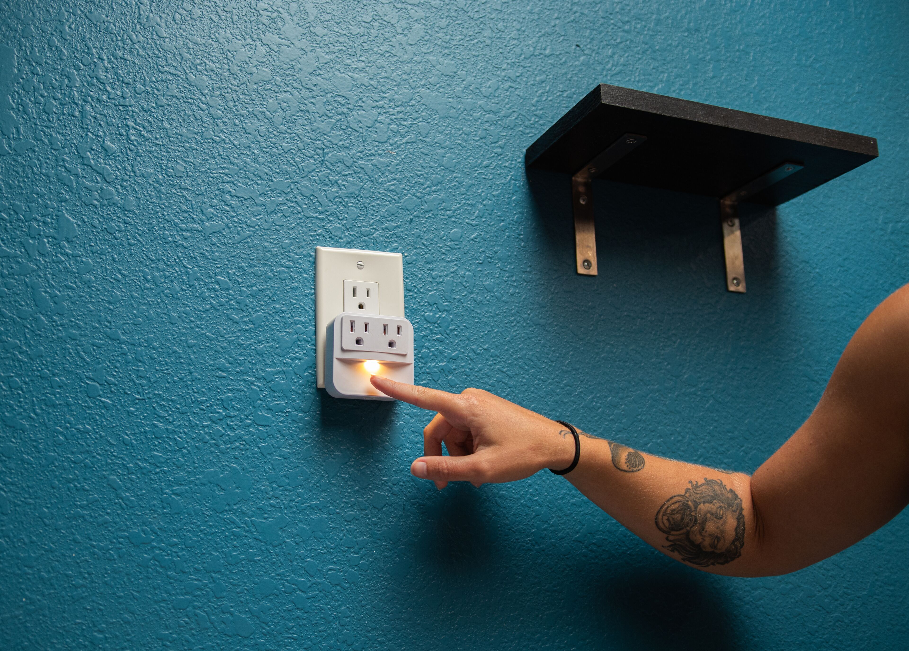 A hand plugging a device into a wall socket on a textured blue wall.