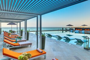 Un espace piscine aménagé sur le toit, avec des chaises longues et des parasols, offrant une vue sur une étendue d’eau.