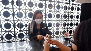 A reception desk with a patterned metal backdrop, a name tag on the counter, and a no smoking sign. - News Front One Hotel Surabaya (Sidoarjo)