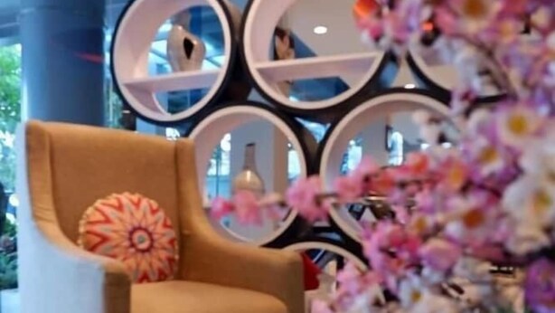 A modern hotel lobby with a comfortable armchair, decorative mirrors, and a glass table with a floral centerpiece. - News Front One Hotel Surabaya (Sidoarjo)