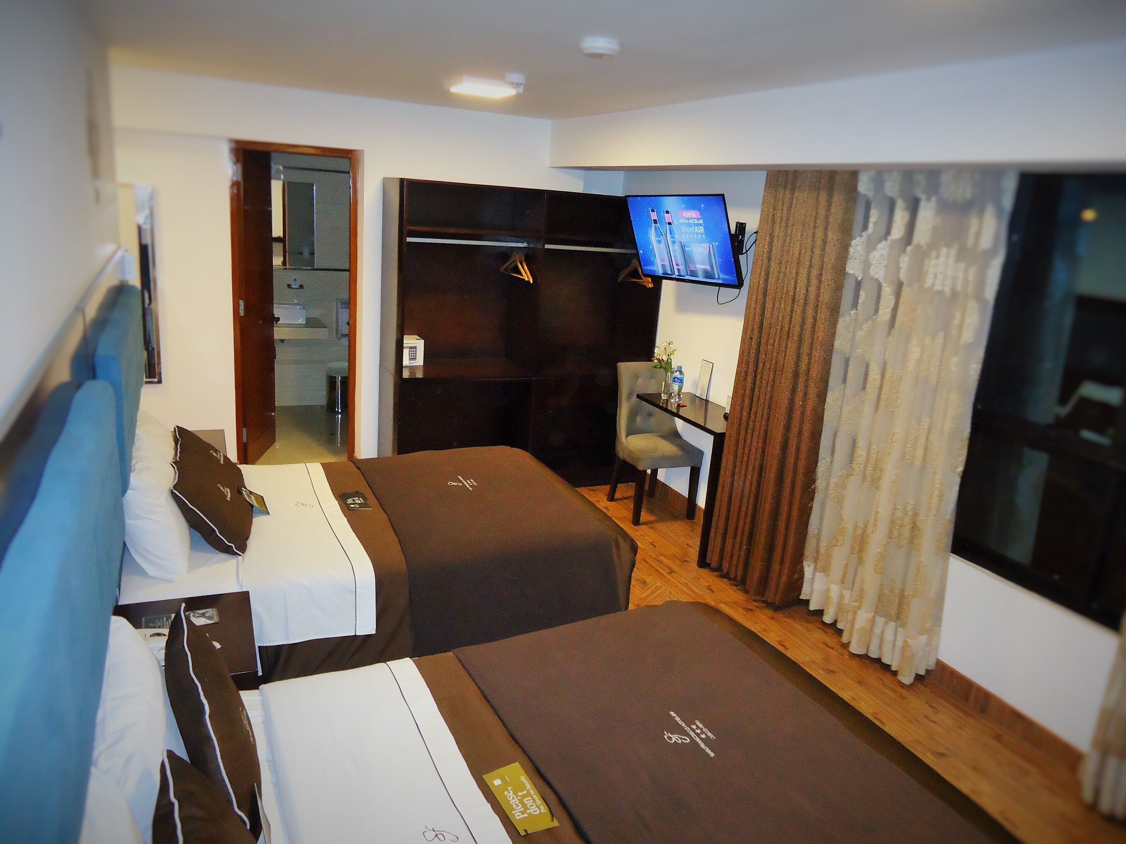 Camera d'albergo con due letti, una scrivania, una TV e un bagno visibile attraverso una porta aperta.