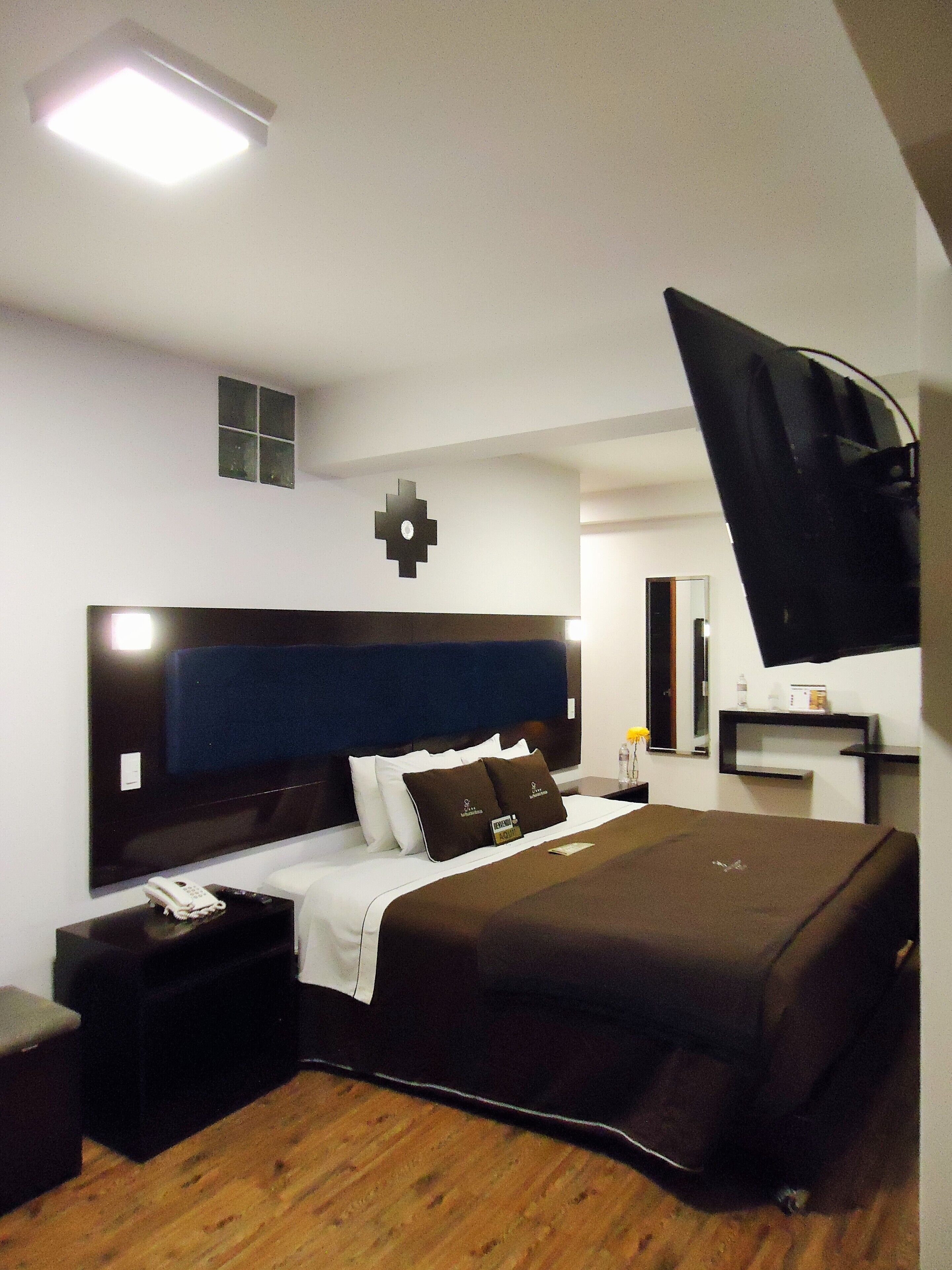 Une chambre d’hôtel moderne avec un grand lit, une table de chevet avec un téléphone, un téléviseur à écran plat fixé au mur et une petite fenêtre.