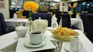 A dining table set with a teapot, cups, a basket of bread, and a spoon. - San Francisco Cusco Hotel (Cusco)