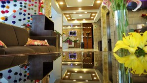 A lobby with a reflective floor, a sofa with patterned cushions, a vase with yellow flowers, and a wall with hanging decorations. - San Francisco Cusco Hotel (Cusco)
