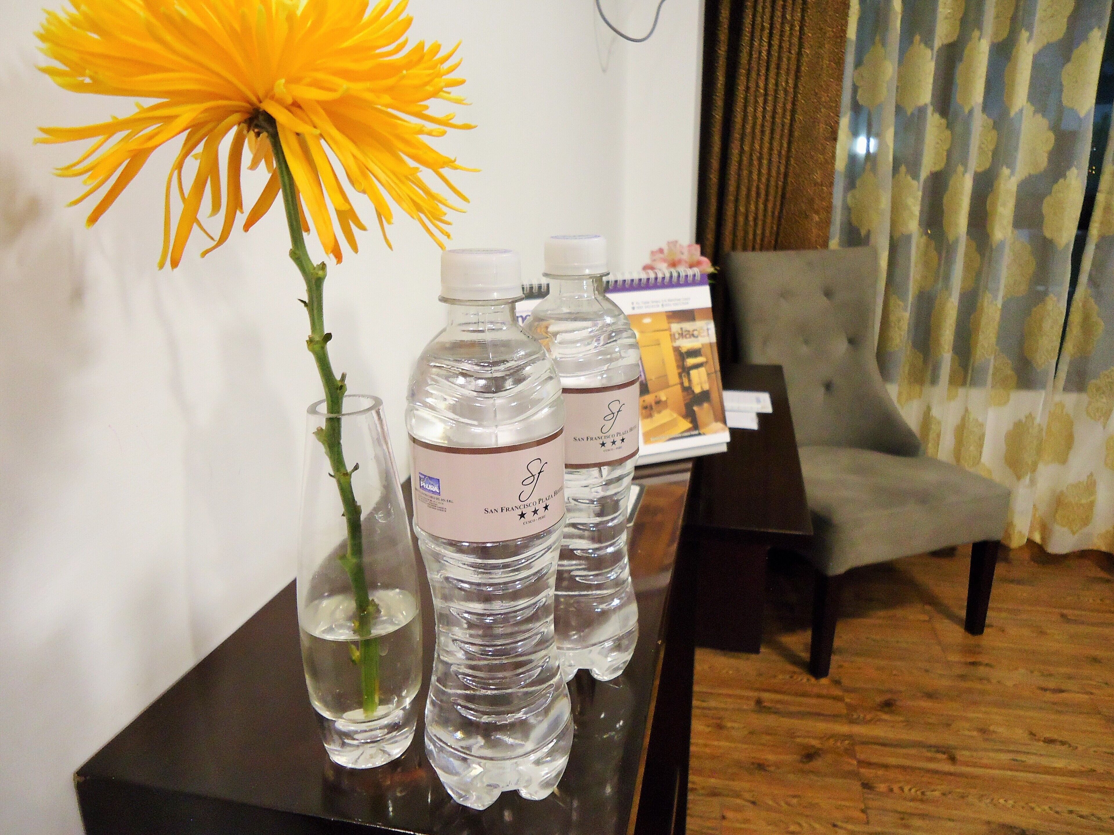 Una mesa con un jarrón de flores amarillas, dos botellas de agua y un vaso.