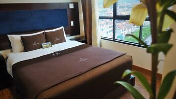 Habitación de hotel con una cama, una mesita de noche, una ventana que ofrece vistas a edificios y una planta en primer plano.