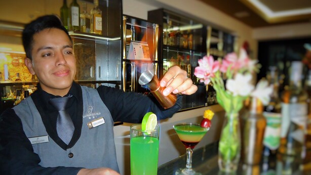 A bartender at a bar with a variety of bottles and glasses. - San Francisco Cusco Hotel (Cusco)