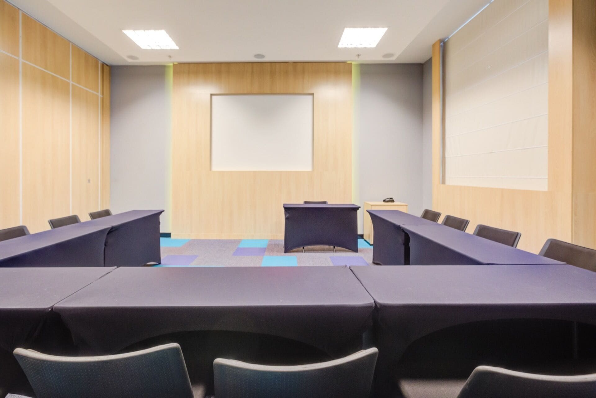 A conference room with a long table, chairs, a projector screen, and a wooden panel wall.