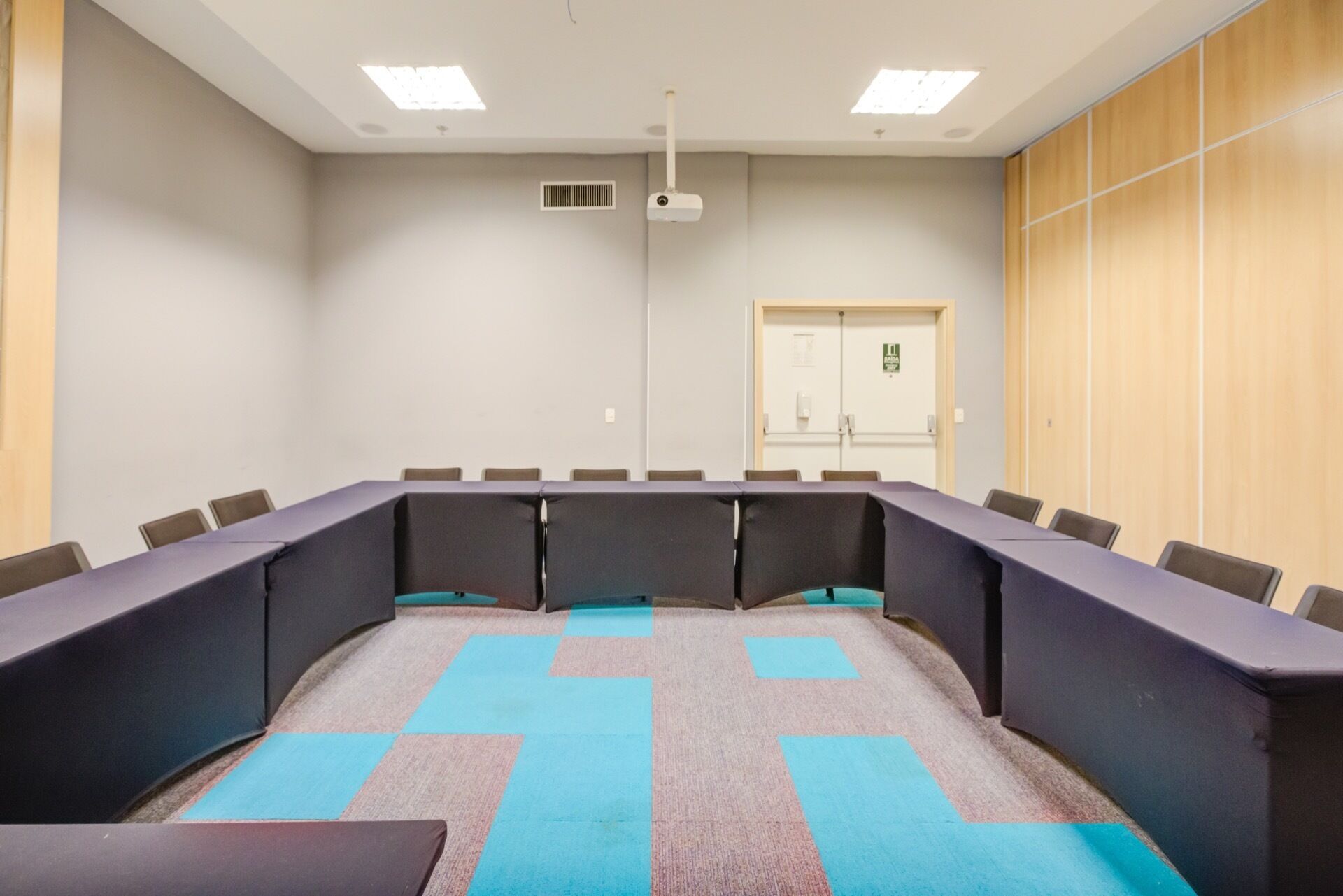A conference room with a long table, chairs, a projector, and a door with a sign.