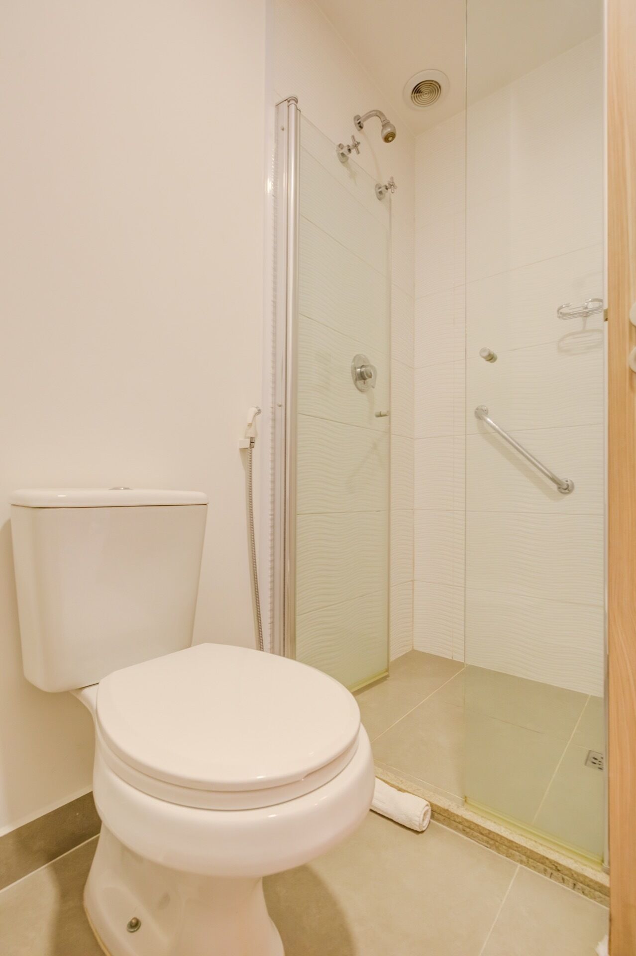 Ein Badezimmer mit Toilette, einer Duschkabine und einem weißen Fliesenboden.