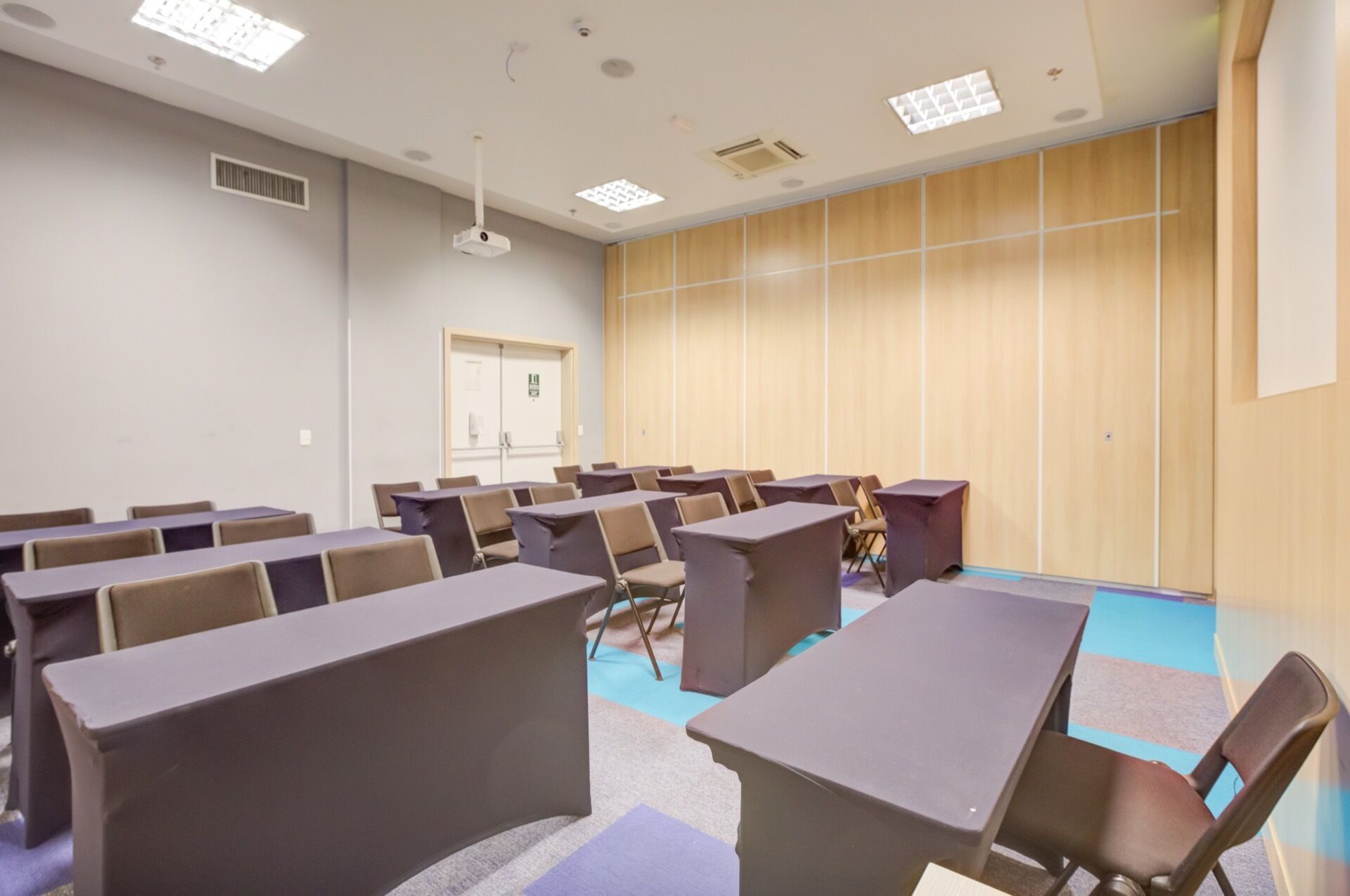 A conference room with rows of tables and chairs, a projector, and a door with a phone.
