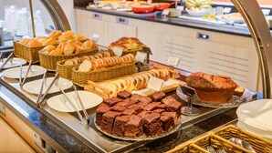 Um buffet com diversos pães, muffins e brownies.