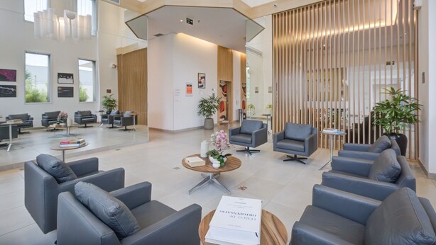 Uma área de recepção moderna com um espaço de estar central, divisória de madeira e uma grande janela que proporciona iluminação natural.