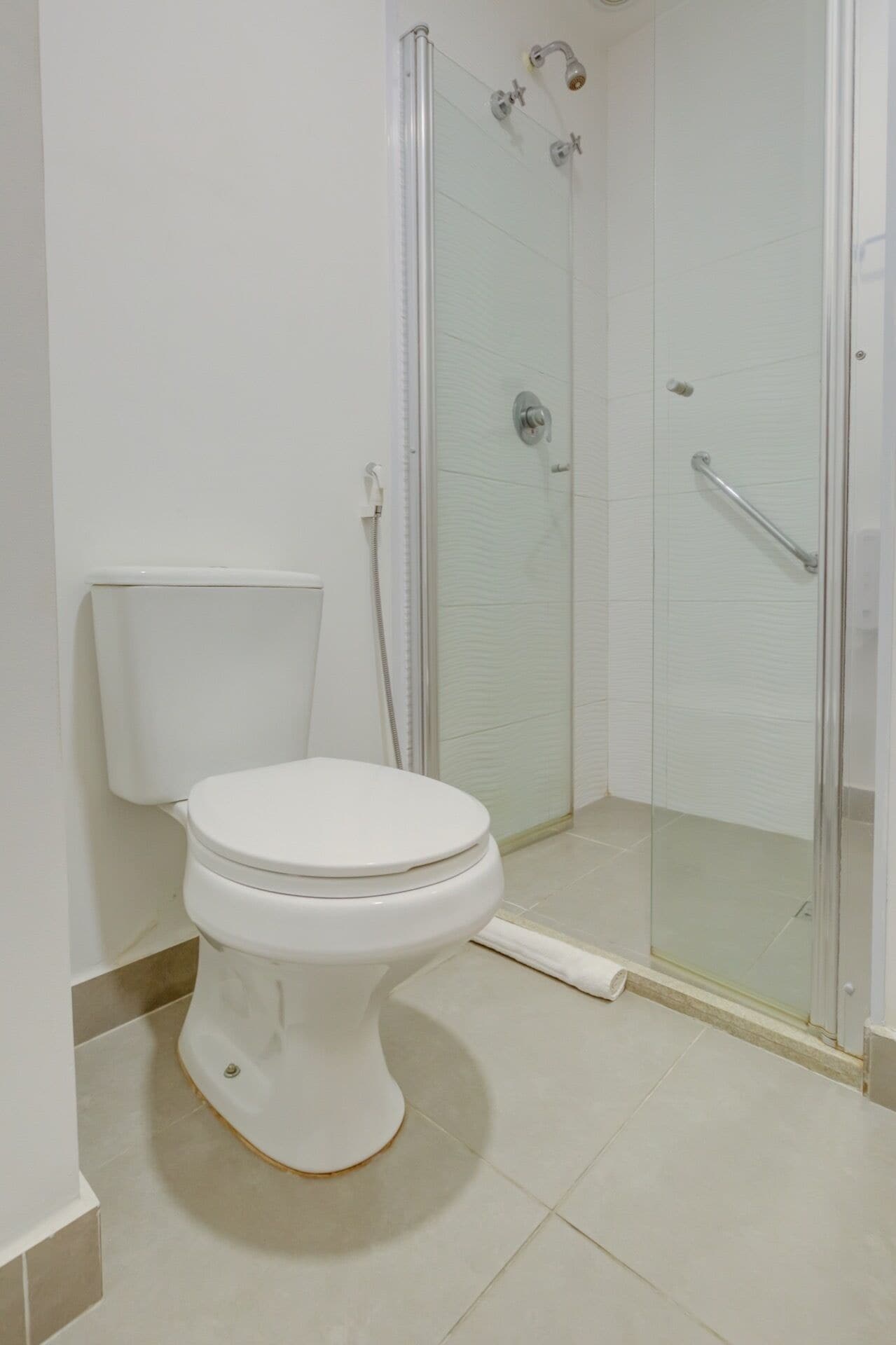 Um banheiro com vaso sanitário, box de chuveiro de vidro e piso revestido de azulejos brancos.