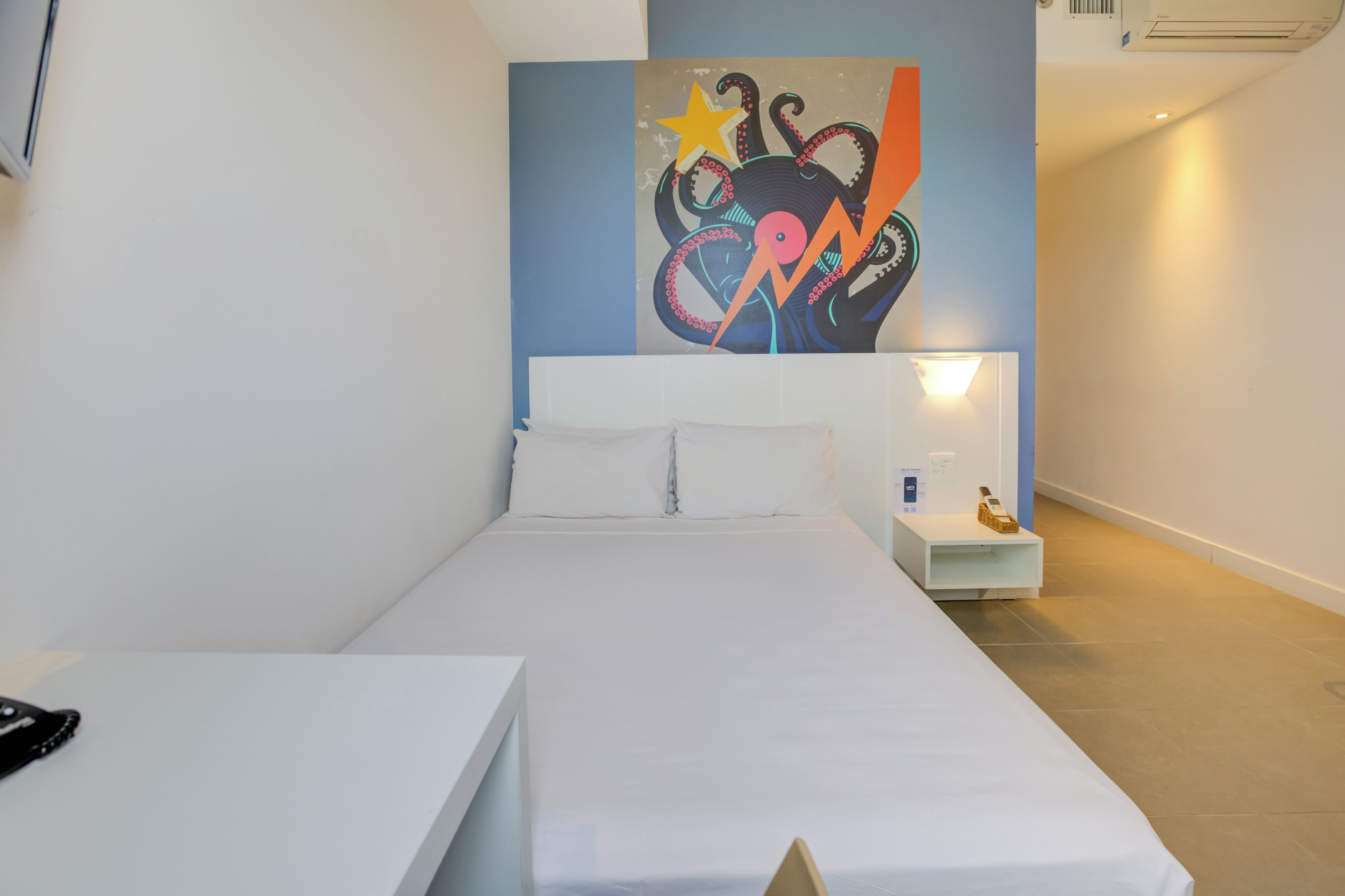Une chambre d’hôtel moderne avec un grand lit, une table de chevet, une petite table et une œuvre d’art accrochée au mur.