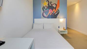 Une chambre d’hôtel moderne avec un grand lit, une table de chevet, une petite table et une œuvre d’art accrochée au mur.