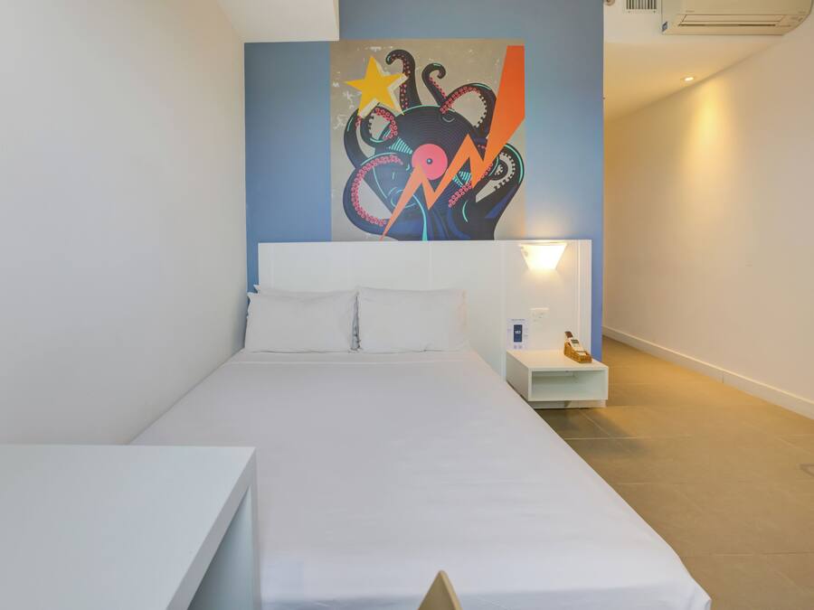 Une chambre d’hôtel moderne avec un grand lit, une table de chevet, une petite table et une œuvre d’art accrochée au mur.