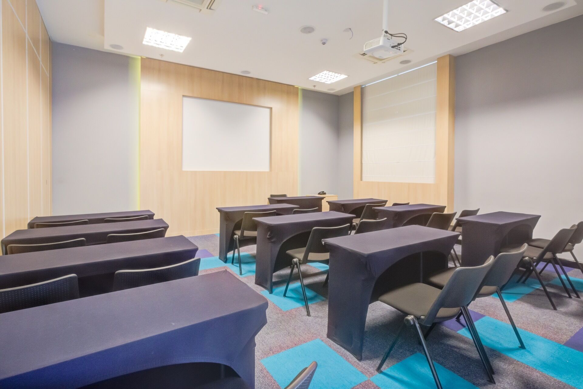 A conference room with multiple tables and chairs, a whiteboard, and a projector screen.
