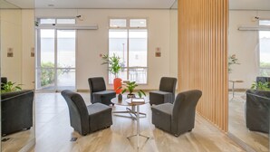 Um hall moderno com poltronas cinzas, uma mesa central e plantas em vasos.