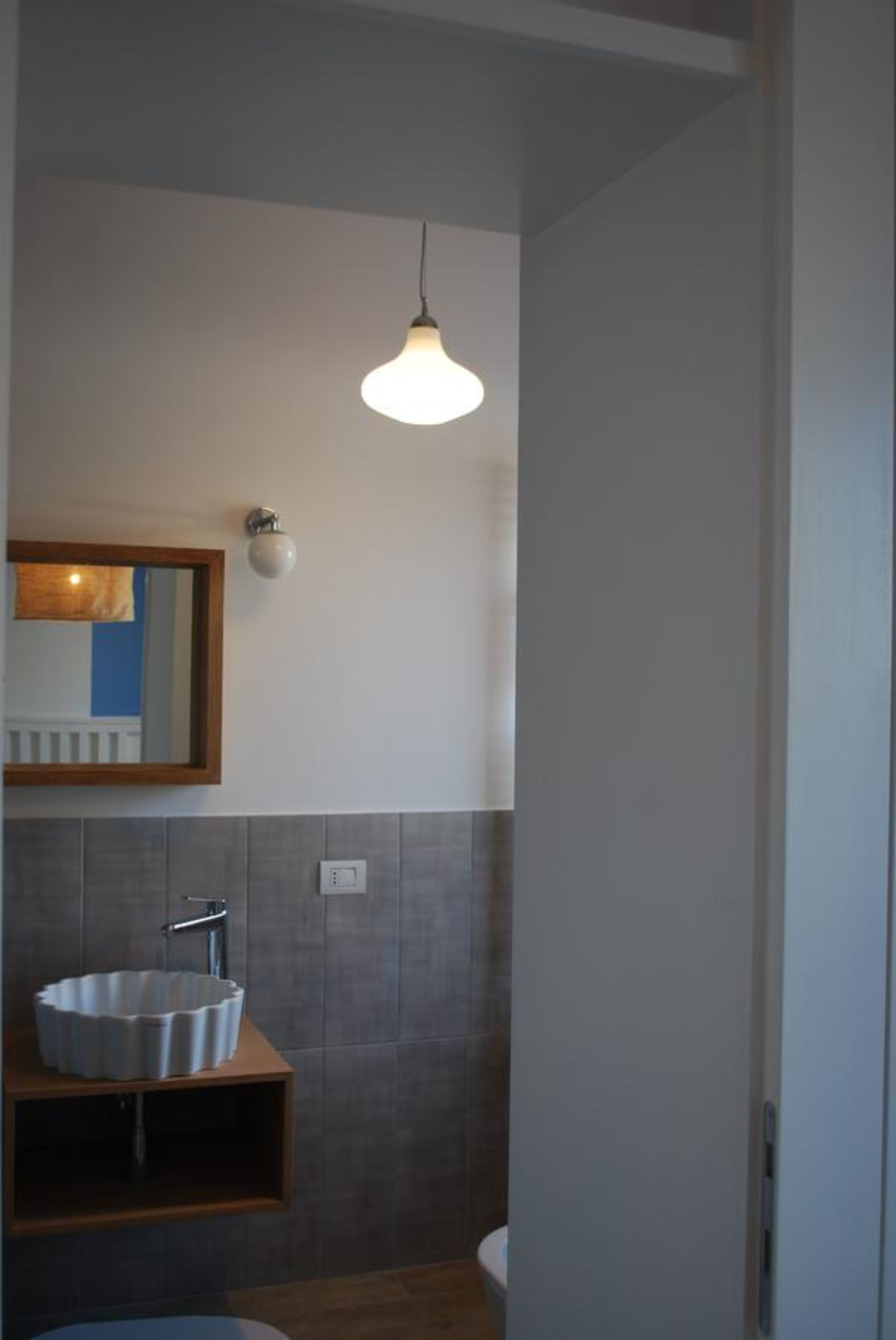 A modern bathroom with a white sink, a mirror, and a pendant light.