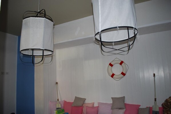 Una habitación con dos lámparas colgantes, un adorno de flotador salvavidas y una cama con almohadas rosas y grises.