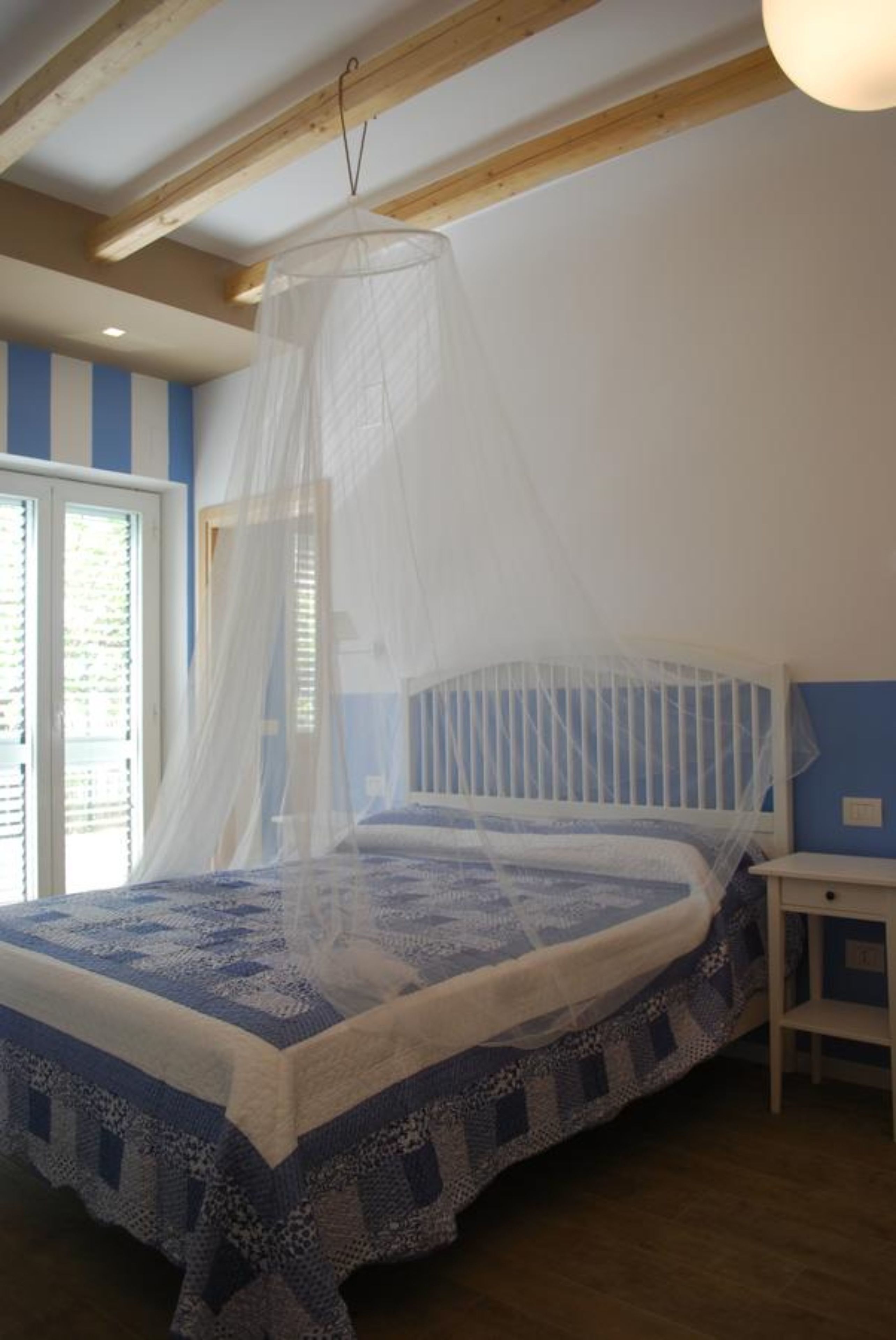 Camera da letto con un letto coperto da un baldacchino bianco, una testiera in legno e una finestra con persiane.