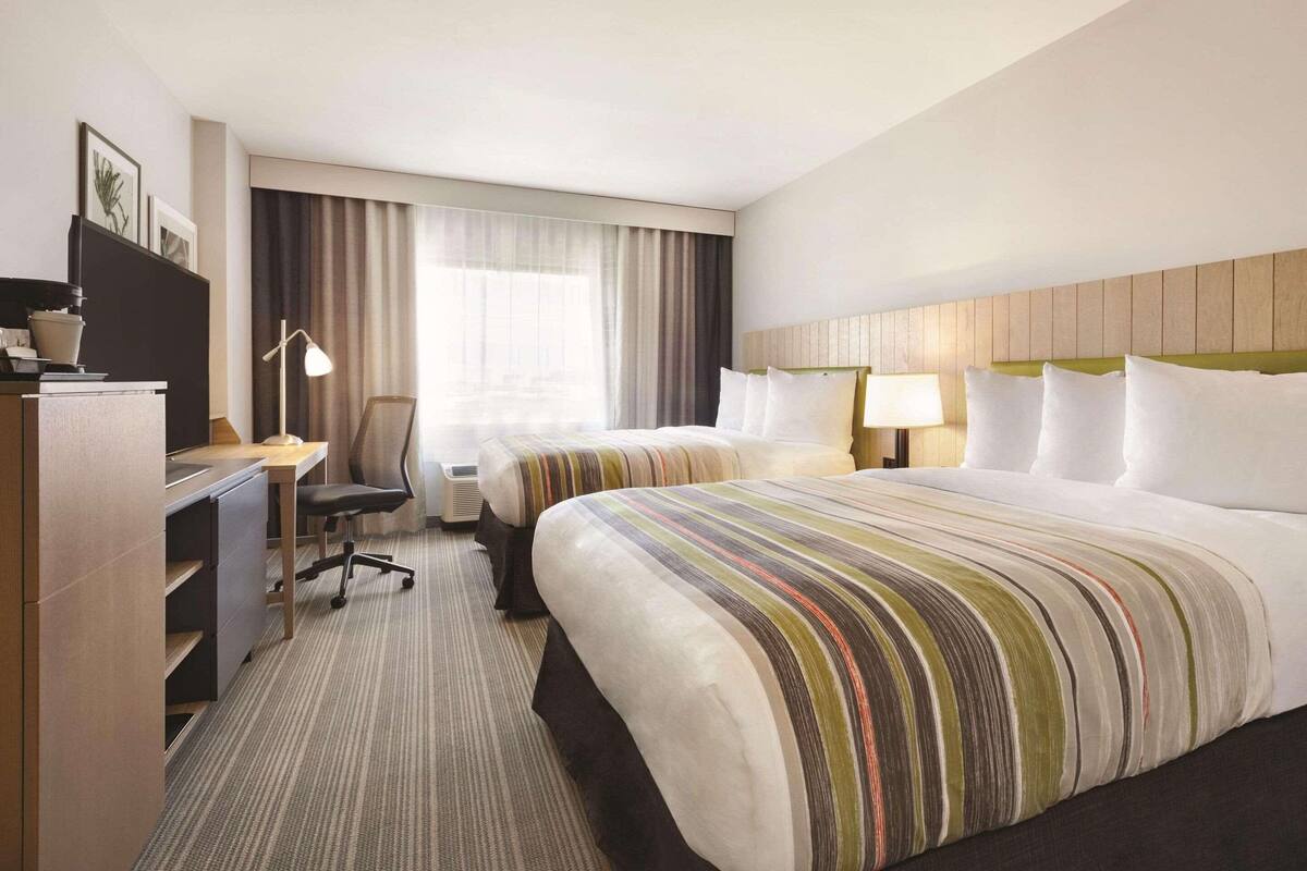 A hotel room with two beds, a desk, a chair, and a large window with curtains.