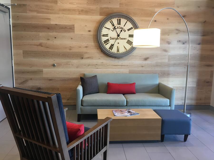 A modern living room with a wooden wall, a round clock, a sofa, a coffee table, and a floor lamp.