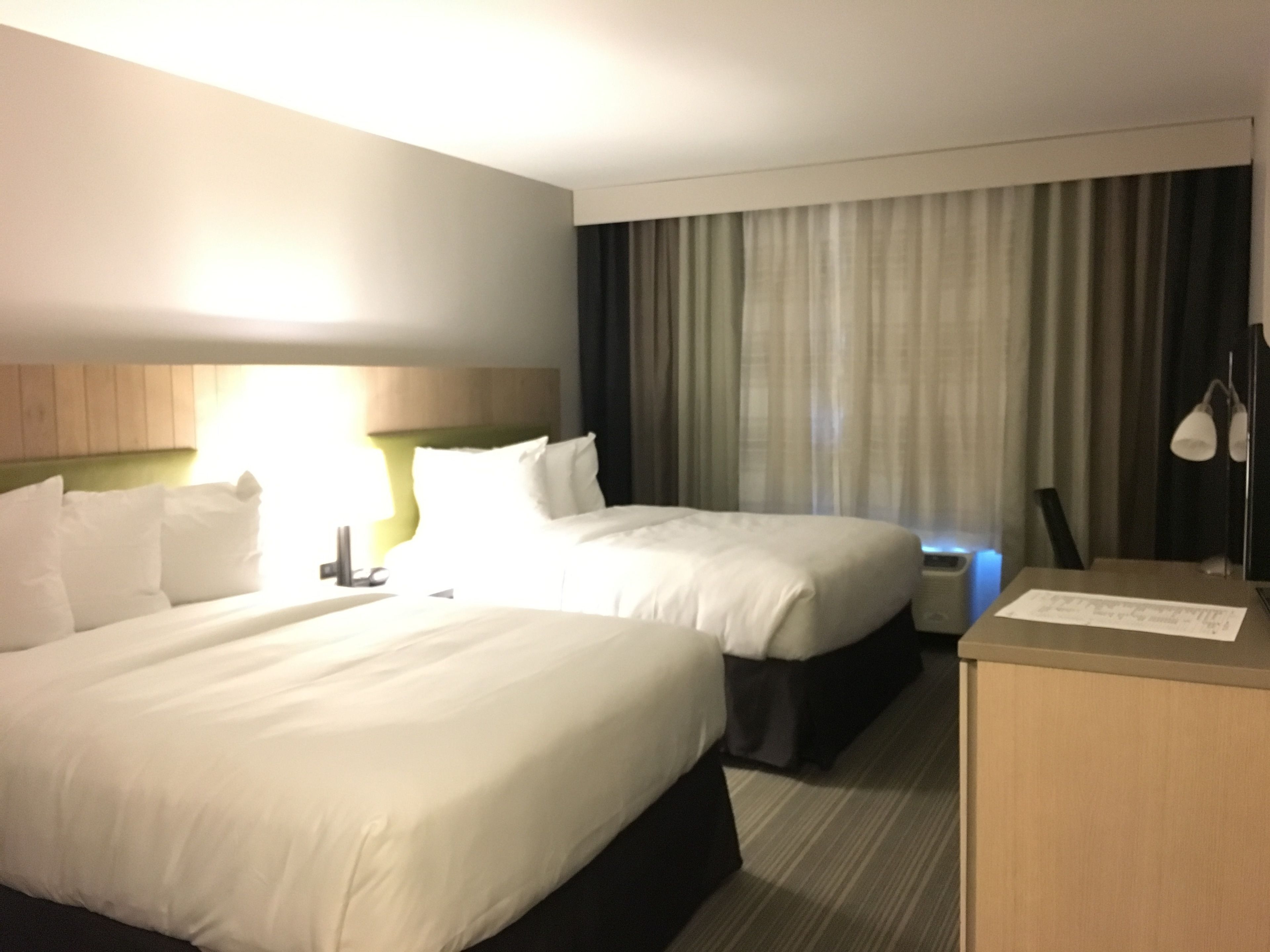 A hotel room with two beds, a desk, a lamp, and a curtain.