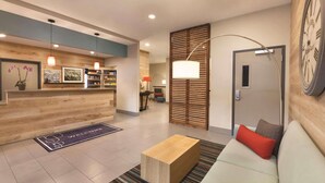 A modern reception area with a wooden reception desk, a sofa with cushions, a coffee table, and a large wall clock. - Country Inn & Suites by Radisson, Ocean City, MD (Ocean City)