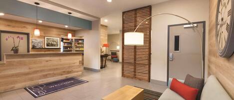 A modern reception area with a wooden reception desk, a sofa with cushions, a coffee table, and a large wall clock.