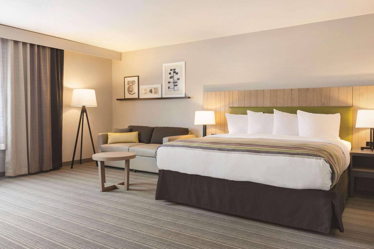 A hotel room with a large bed, a sofa, a small table, and two bedside lamps.