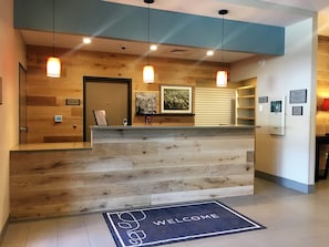 Un mostrador de recepción con detalles de madera, un tapete de bienvenida y un quiosco de registro.